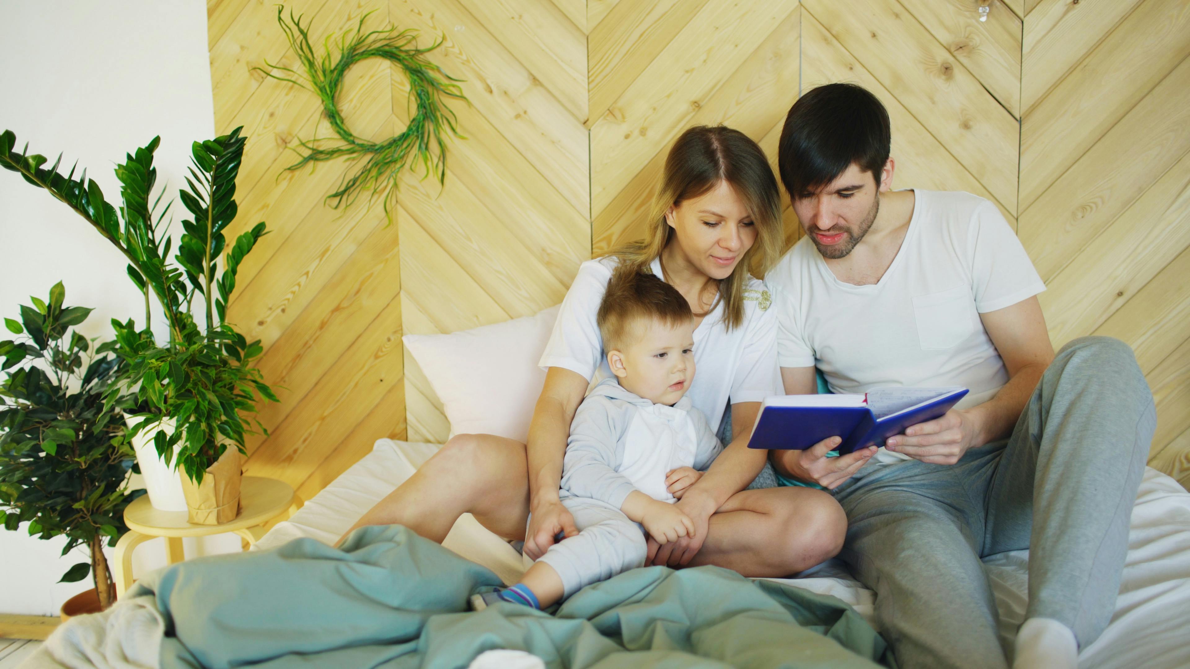 Loving parents reading a book with their child in a cozy bedroom setting, promoting family bonding.